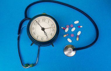 Hapların zamanında alınması için çalar saat, steteskop, çok renkli haplar, mavi arka planda..