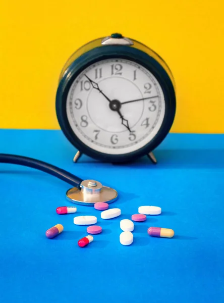 Autumn colds. Time to take pills. Alarm clock, stethoscope, colorful pills, autumn leaves of different colors on a wooden table.