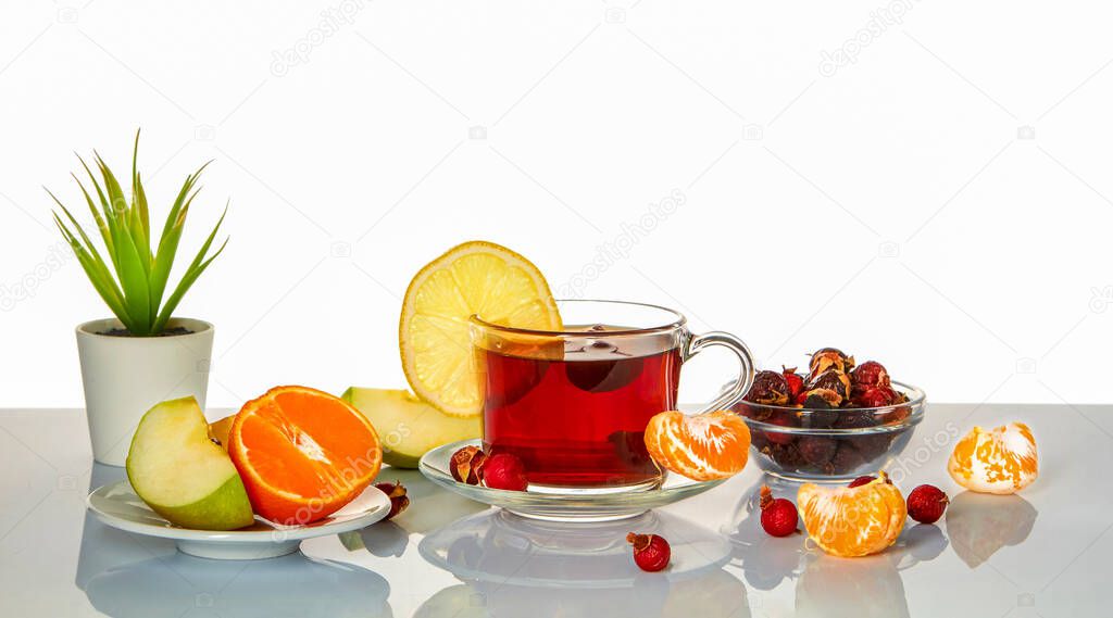Cup with rosehip infusion, apple, lemon and mandarin on a mirror surface.