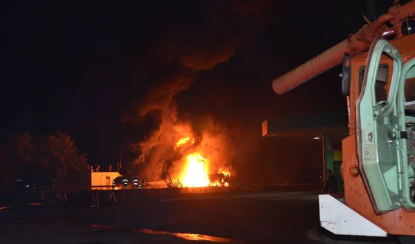 This is a photo of a big night fire accident with explosion. A truck with dangerous cargo exploded and caught fire. Firemen start fight the fire.