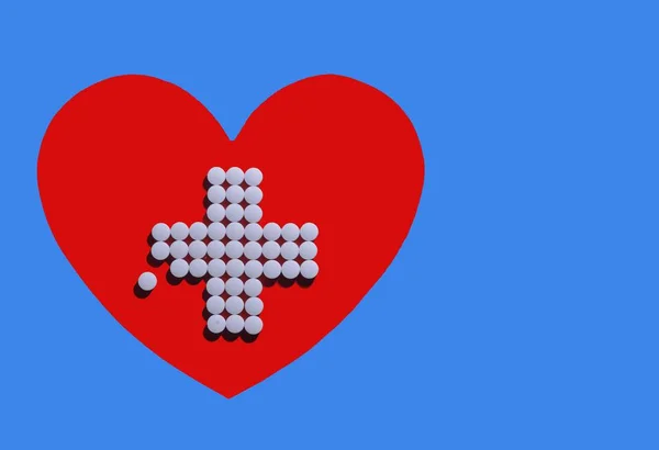 青い背景の前の赤い心臓に白い錠剤で作られた十字架 左側のタブレットは薬局 薬店のロゴとして使用できます — ストック写真