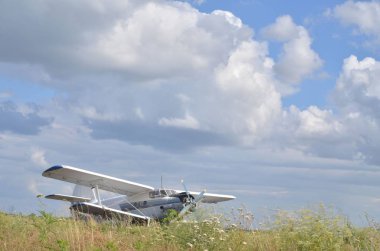 Pictured is an old airplane, a biplane, which stands on the field. A nice summer day, light clouds in the sky. A pleasant, light image. May be the background.
