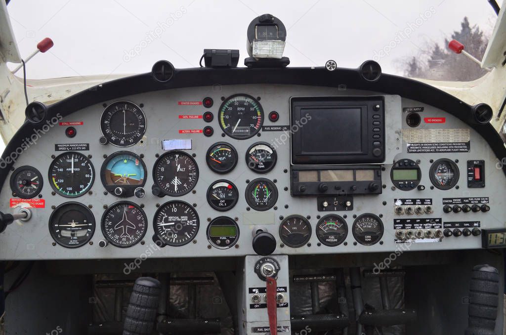 The front panel of a small airplane is shown in the photo. Instruments, lights, indicators, a control knob and pedals are visible on the panel.