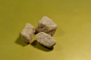 Three pieces of brown sugar. are placed on a gold background.