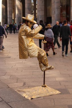 Milan, İtalya - 16 Nisan 2017: Altın kostümlü maskeli bir sokak sanatçısı Piazza del Duomo Meydanı 'nda havada asılı duran bir heykel gibi davranıyor.