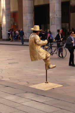 Milan, İtalya - 16 Nisan 2017: Altın kostümlü maskeli bir sokak sanatçısı Piazza del Duomo Meydanı 'nda havada asılı duran bir heykel gibi davranıyor.