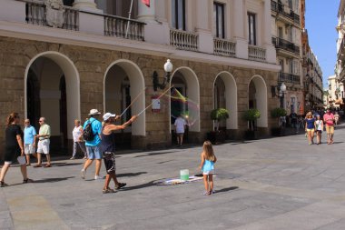 Cadiz, Endülüs, İspanya - 5 Ağustos 2017: Bilinmeyen bir sanatçı, Plaza de San Juan de Dios Meydanı 'nda iki çubuk ve iplikle büyük sabun köpükleri yapıyor.