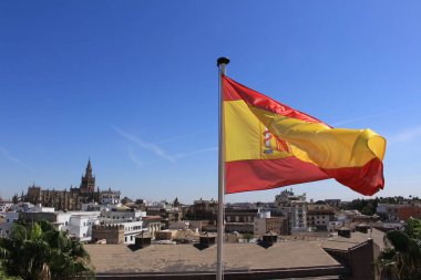 Sevilla Katedrali 'nin (Seville Katedrali) havadan görünüşü ve İspanya' nın Seville kentindeki Altın Kulesi 'nden (Torre del Oro) alınan rüzgarda dalgalanan bir İspanyol bayrağı ile eski şehir merkezi..