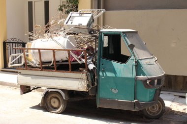 CHANIA, CRETE ISLAND, GREECE - AUGUST 3, 2016: An old three-wheeled commercial car full of broken devices, scraps and rubbish at Mitropolitou Kyrillou street. 