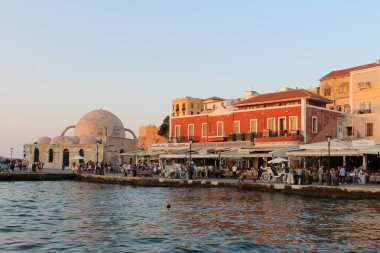 CHANIA, CRETE ADA, GREECE - 28 Temmuz 2016: Kucuk Hasan Paşa Camii ve turistlerle dolu eski Venedik limanı manzarası ve gün batımında Akti Tompazi Caddesi 'ndeki güzel tarihi binalar.