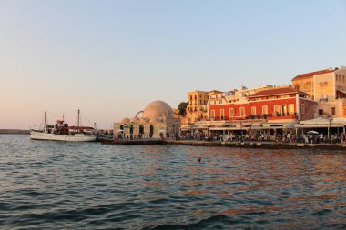 CHANIA, CRETE ADA, GREECE - 28 Temmuz 2016: Kucuk Hasan Paşa Camii ve turistlerle dolu eski Venedik limanı manzarası ve gün batımında Akti Tompazi Caddesi 'ndeki güzel tarihi binalar.