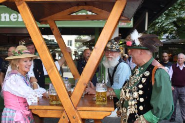 MUNİK, Almanya - 22 AĞUSTOS 2015: Geleneksel Alman giysileri içindeki insanlar eski gıda pazarında bira içiyorlar 