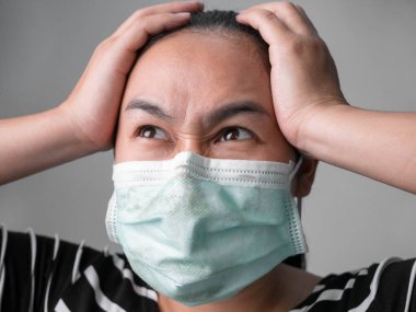 Hava kirliliğinden ya da gri arka planda virüs salgınından korunmak için yüz maskesi takan stresli genç bir kadın. Sağlık hizmeti kavramı.