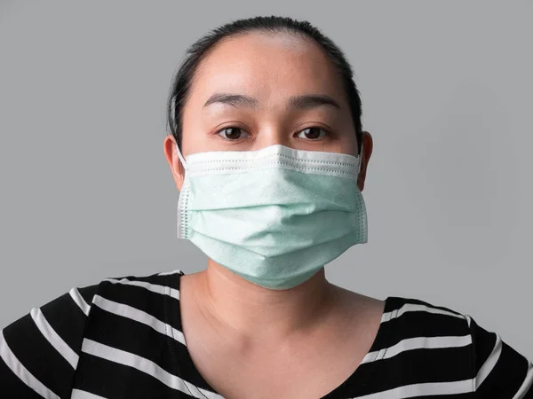 Fatigued Asian woman wearing facial mask for protection from air pollution or virus epidemic on grey background.