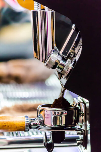 Espresso machine grinding roasted coffee bean into tamper.
