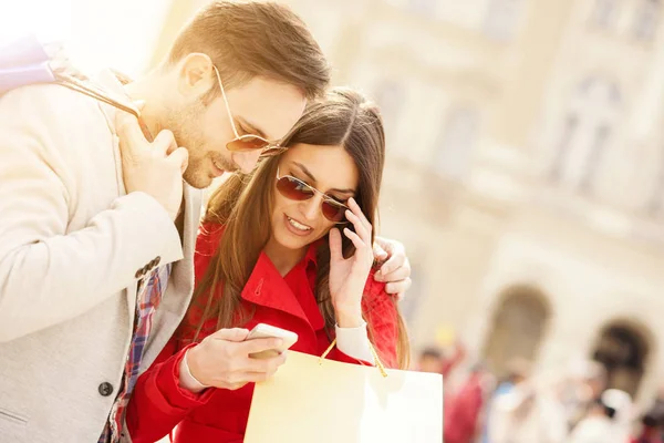 Joven pareja feliz con teléfono inteligente y bolsas de compras en la ciudad —  Fotos de Stock