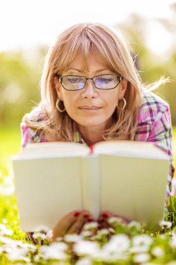 Mutlu kadın park ilkbaharda sırasında bir kitap okuma
