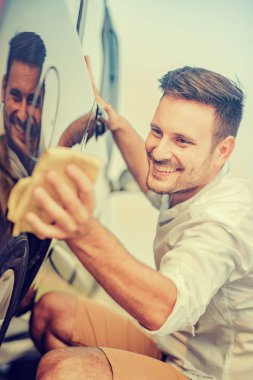 Genç adam arabasını dışarıda temizliyor.