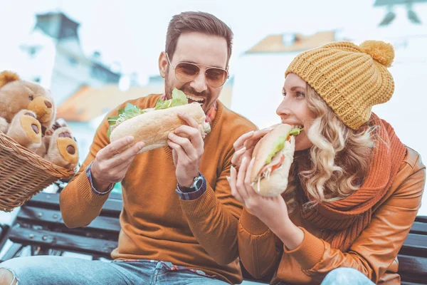 Joyeux jeune couple manger un sandwich à l'extérieur — Photo