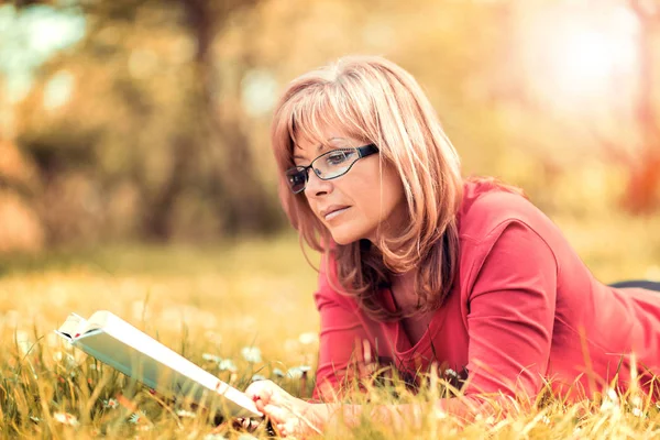 Жінка читає книгу в парку на траві — стокове фото