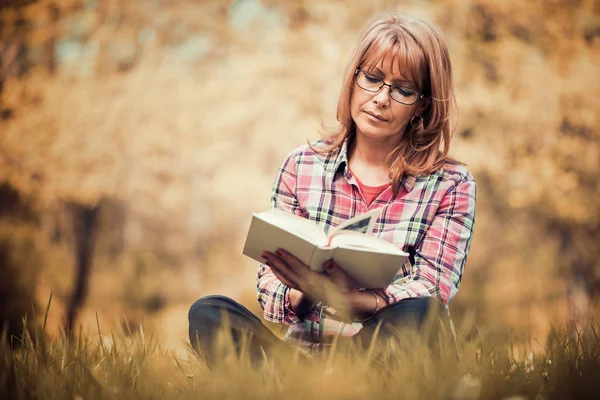 Mulher lendo livro no parque na grama — Fotografia de Stock