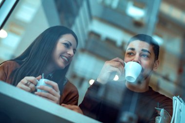 Bir pencere tarafından kafede oturan ve gülen genç Çift