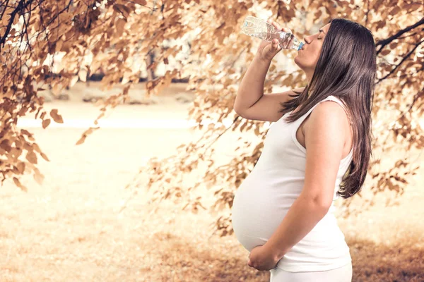 Беременная женщина пьет воду из бутылки — стоковое фото