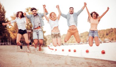 Mutlu gençler plajda zıplıyorlar.