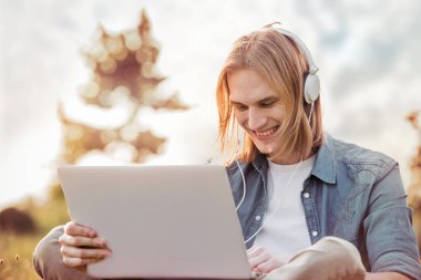 Mutlu genç adam parkta dizüstü bilgisayar kullanarak