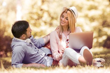 Genç çift parkta dizüstü bilgisayar kullanarak