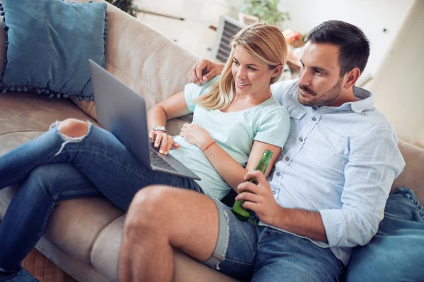 Couple on sofa with laptop and beer