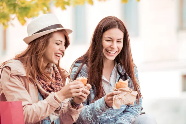 Dos hermosas chicas comiendo sándwiches después de ir de compras . — Foto de Stock