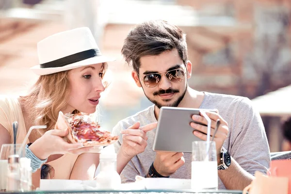 Pareja comiendo pizza en la cafetería y mirando en la tableta . — Foto de Stock