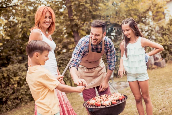 Gelukkige jonge familie barbecueën vlees op de grill. — Stockfoto