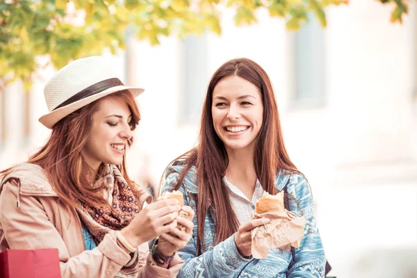 Dos amigas jóvenes se ríen y comen sándwich al aire libre . — Foto de Stock