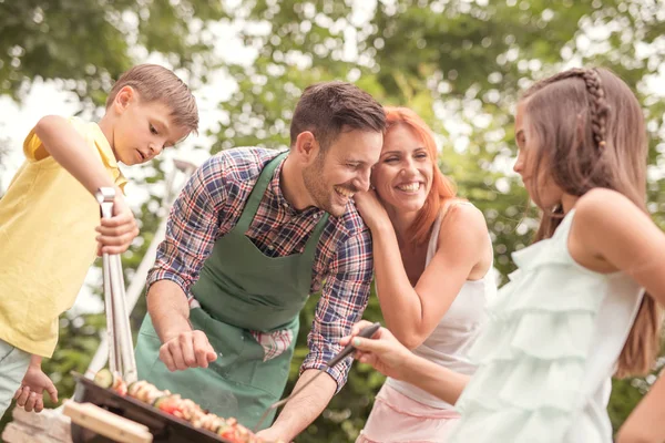 Pai ensinando filho cozinhar em churrasco com a família em backgroun — Fotografia de Stock
