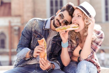 Seven çift sandviç yiyor sokakta.