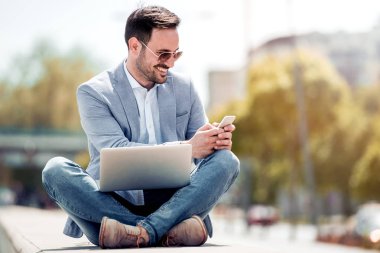 Akıllı telefon kullanırken dışında oturan genç çekici adam