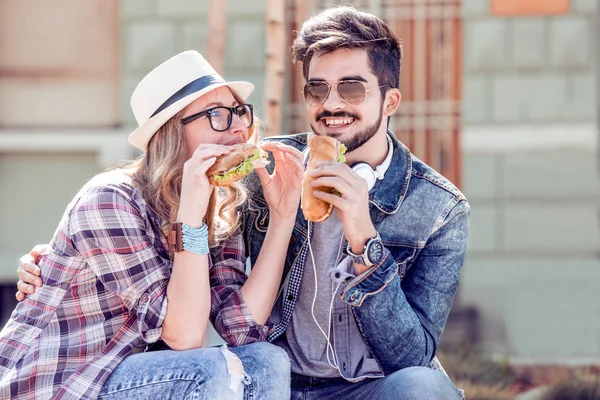 Молодая пара влюблена, парень и девушка сидят и едят сэндвич . — стоковое фото