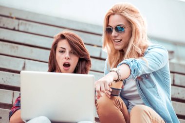 İki güzel mutlu kızı merdivende bir dizüstü bilgisayar kullanarak.