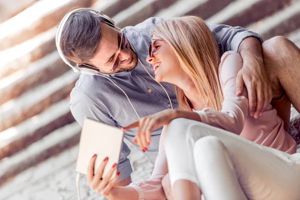 Young couple watching a video on a tablet on the stairs.They smile, seeing the funny video.