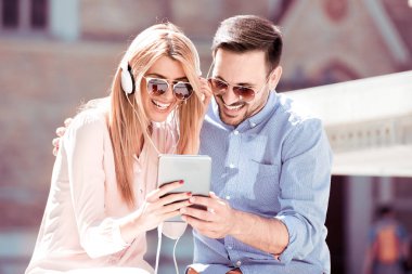Şehir merkezinde oturan ve tablet ile müzik dinlemek genç Çift.