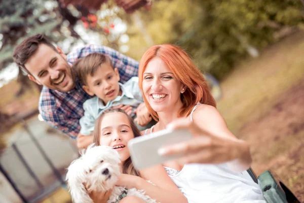 Happy family with dog taking selfie with smart phone in the park.Family, pet, technology and people concept.