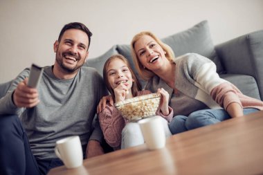 Gülümseyen genç aile birlikte Tv izliyor.