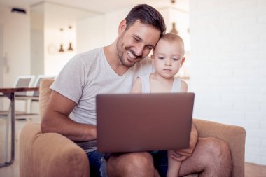 Aile, babalık, teknoloji ve insan kavramı mutlu baba ve küçük oğlu evde koltukta oturan tablet pc bilgisayar ile.