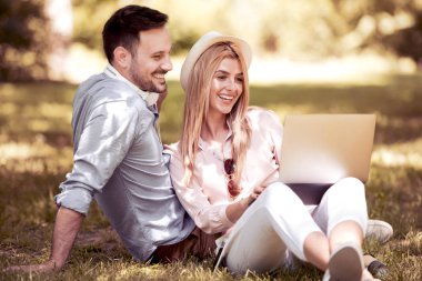 Birlikte yaz günü parkta oturan, dizüstü bilgisayar kullanarak, gülüyor, eğleniyor genç güzel mutlu çift.