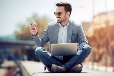 Dışarıda, cep telefonunuzu kullanarak ve dizüstü bacaklar ile otururken görünümlü çekici bir adam geçti.