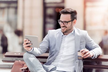 Bir bankta otururken onun Pc tablet kullanarak rahat iş adamı. Dinlenme ve içecek kahve.