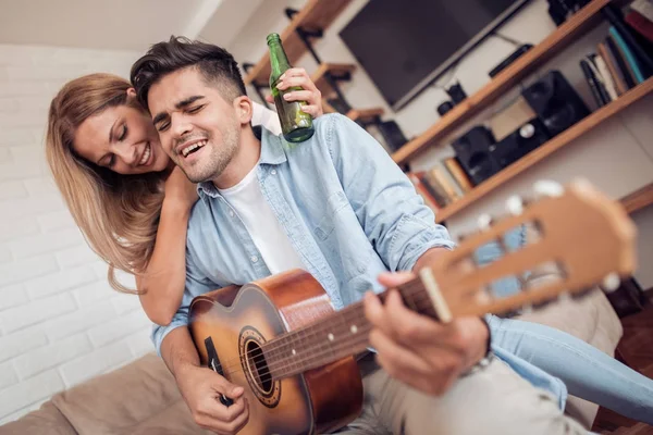 Hombre joven tocando la guitarra de su chica en la sala de estar . — Foto de Stock
