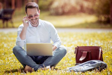 Çimenlerin üzerinde oturan bir dizüstü bilgisayar ile genç adam